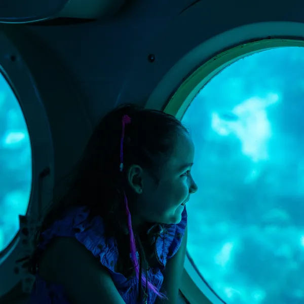 Child looking out of a submarine window at the underwater view.