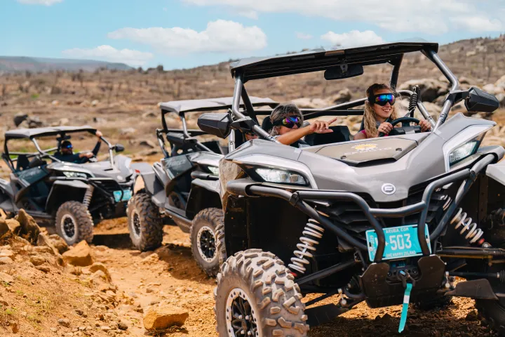 Three off-road vehicles driving on rocky terrain under a blue sky.