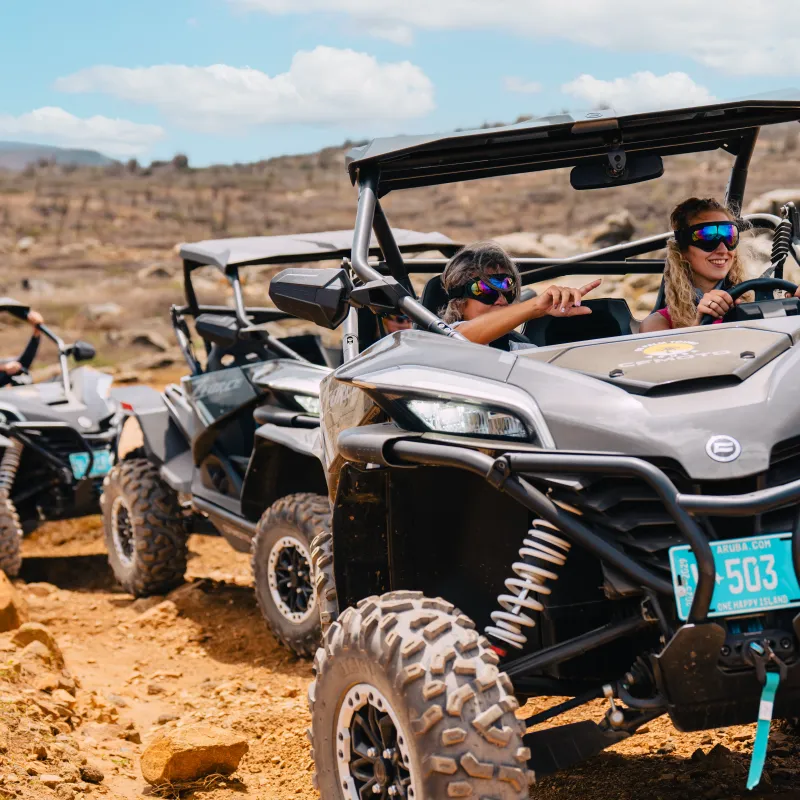 Three off-road vehicles driving on rocky terrain under a blue sky.