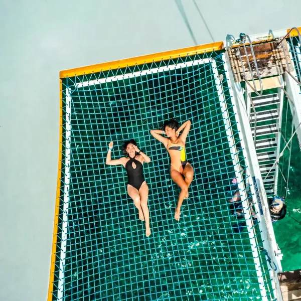 Two people sunbathing on a netted deck above water.