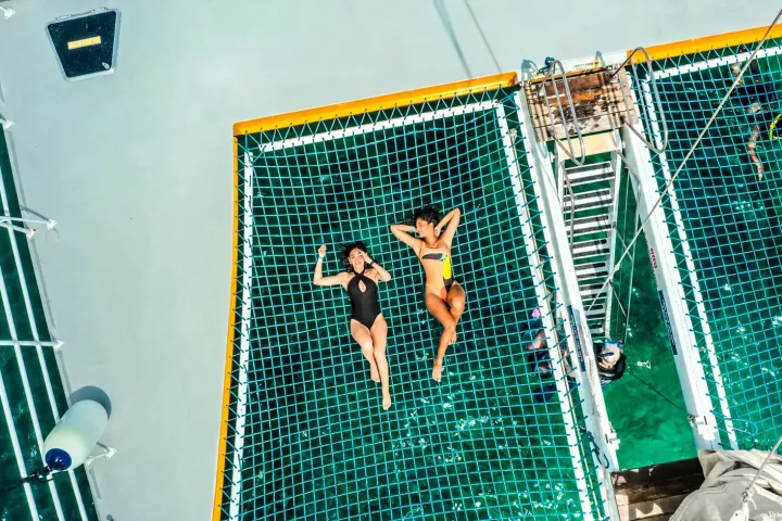 Two people sunbathing on a netted deck above water.