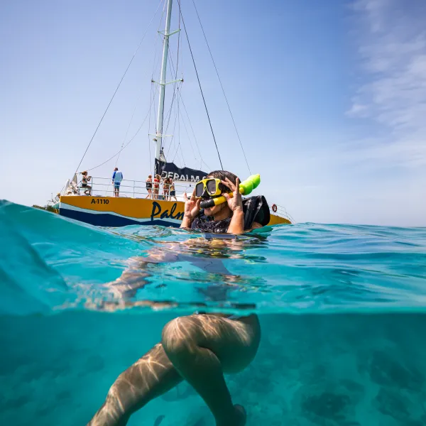 Person snorkeling near a boat in clear blue water.