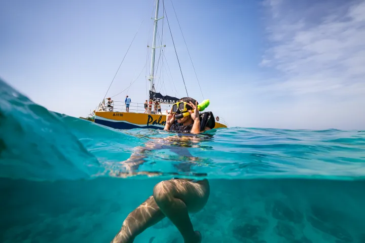 Person snorkeling near a boat in clear blue water.