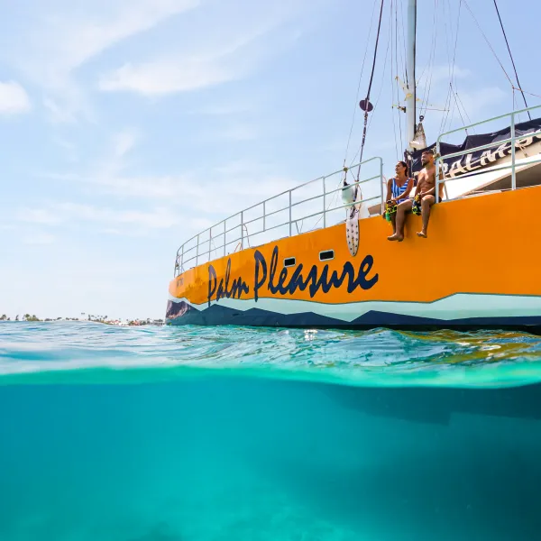 Two people sitting on the edge of a yellow boat above clear blue water.