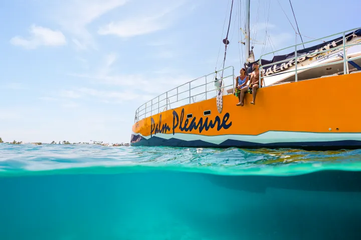 Two people sitting on the edge of a yellow boat above clear blue water.