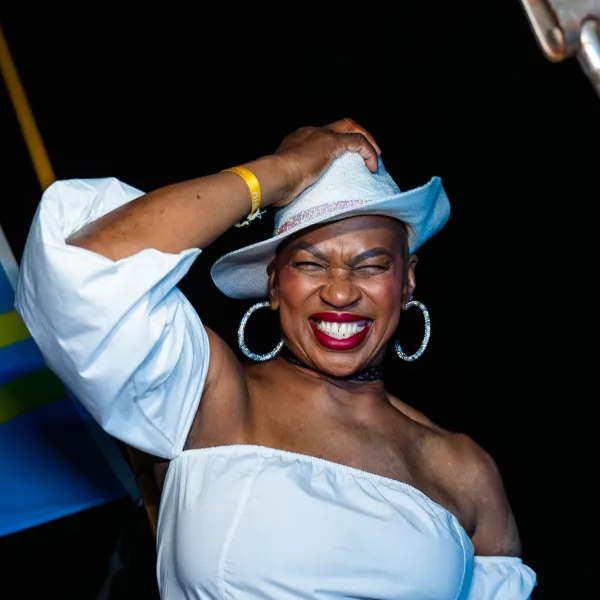 Smiling person in white outfit and hat with flag in background at night.