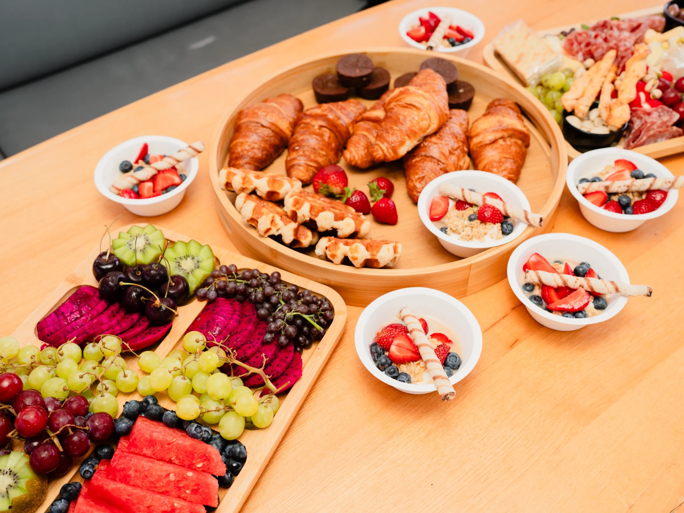 Assorted breakfast foods: croissants, fruit, and cheese on a wooden table.