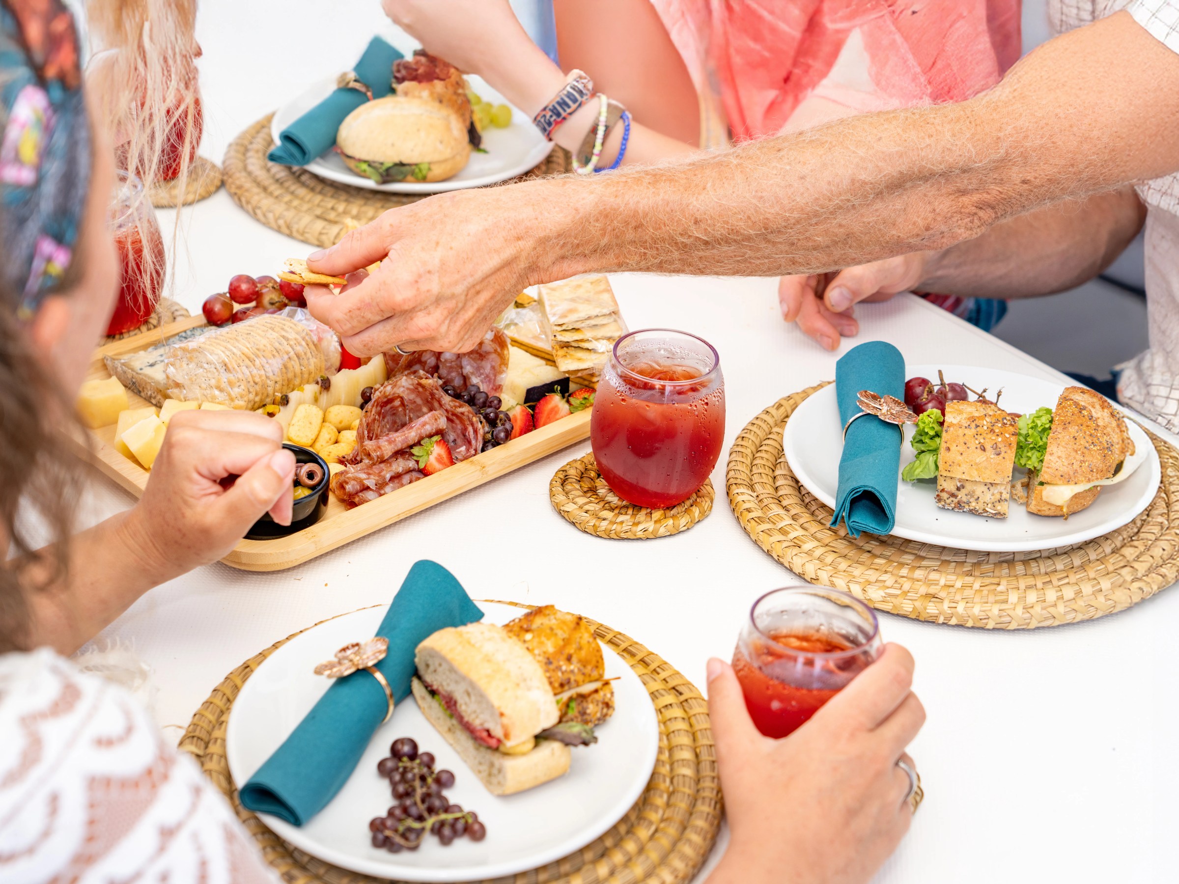 People enjoying a meal with drinks, sandwiches, and a charcuterie board.