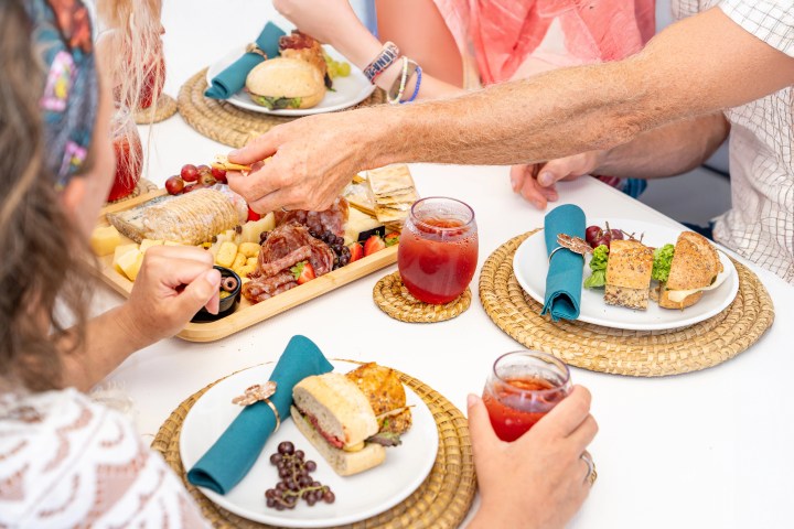 People enjoying a meal with drinks, sandwiches, and a charcuterie board.