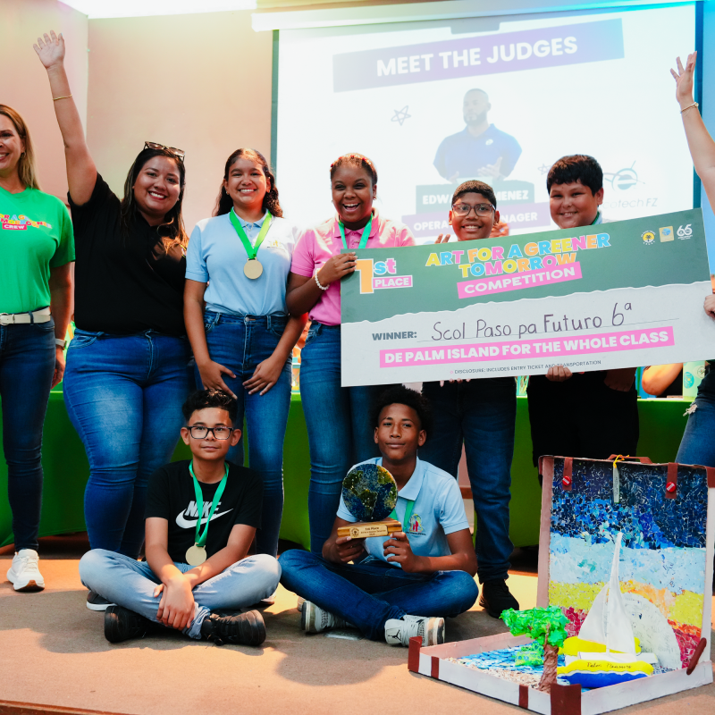 Group of smiling students and adults holding a large check and trophy on stage.