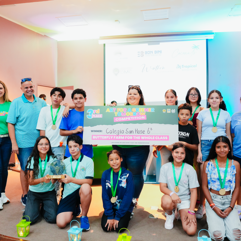 Group of children and adults with banner celebrating art competition win on stage.