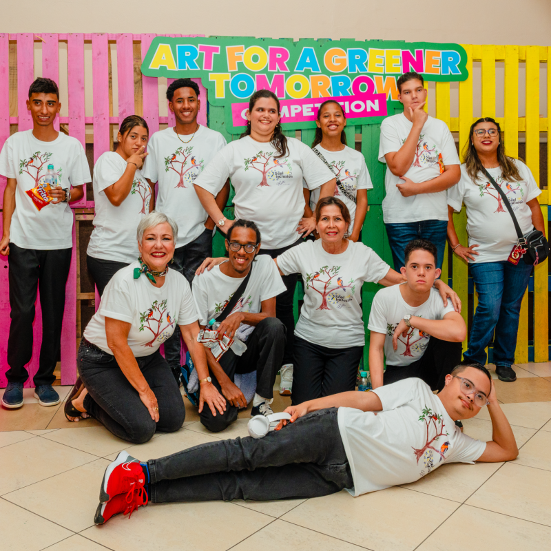 Group of people in matching shirts posing in front of colorful pallets with 'Art for a Greener Tomorrow' sign.
