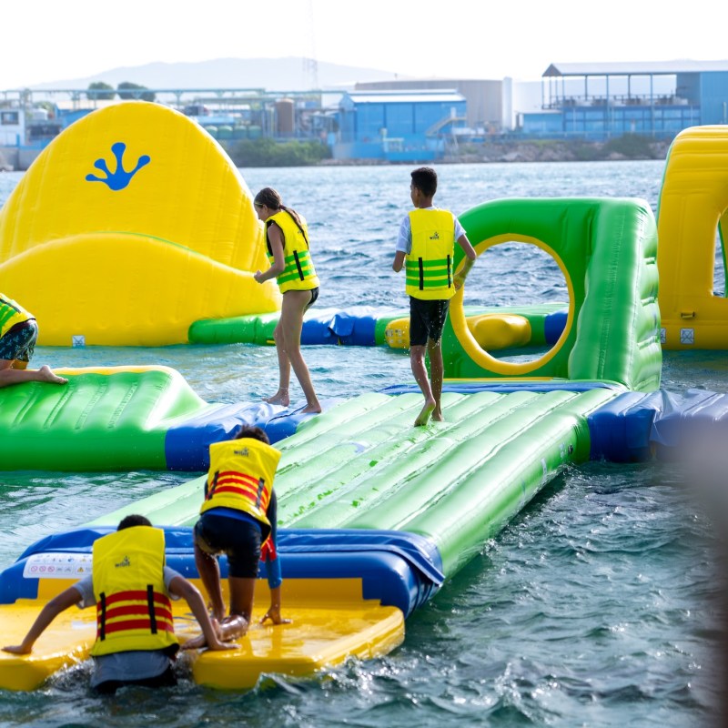 People in yellow vests on an inflatable water obstacle course.