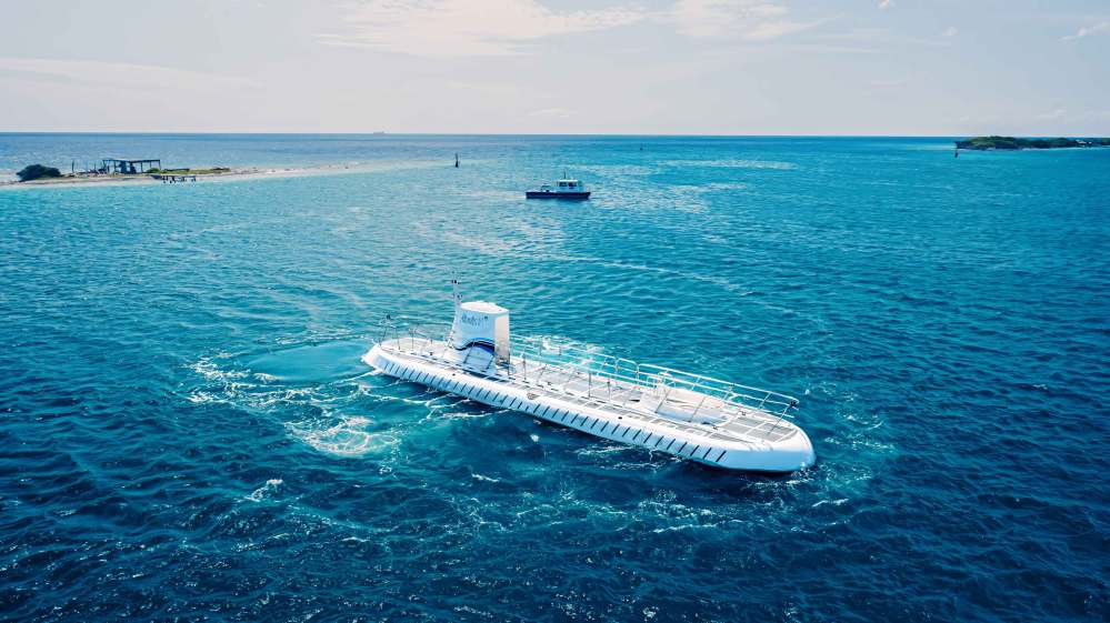 White submarine floating on blue ocean near a small island with clear sky.