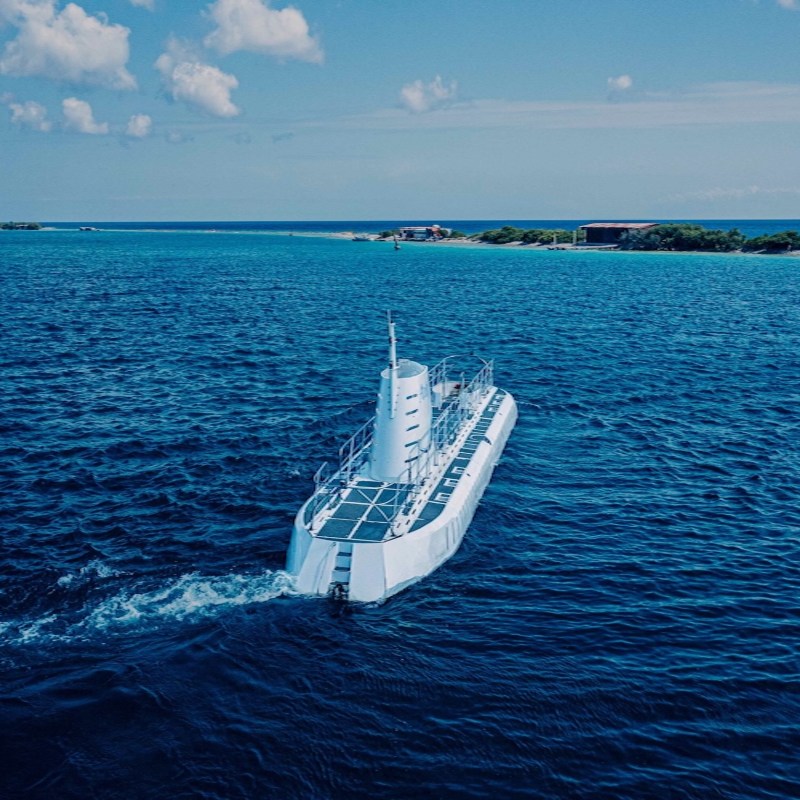 Submarine cruising on blue ocean with distant islands under a partially cloudy sky.