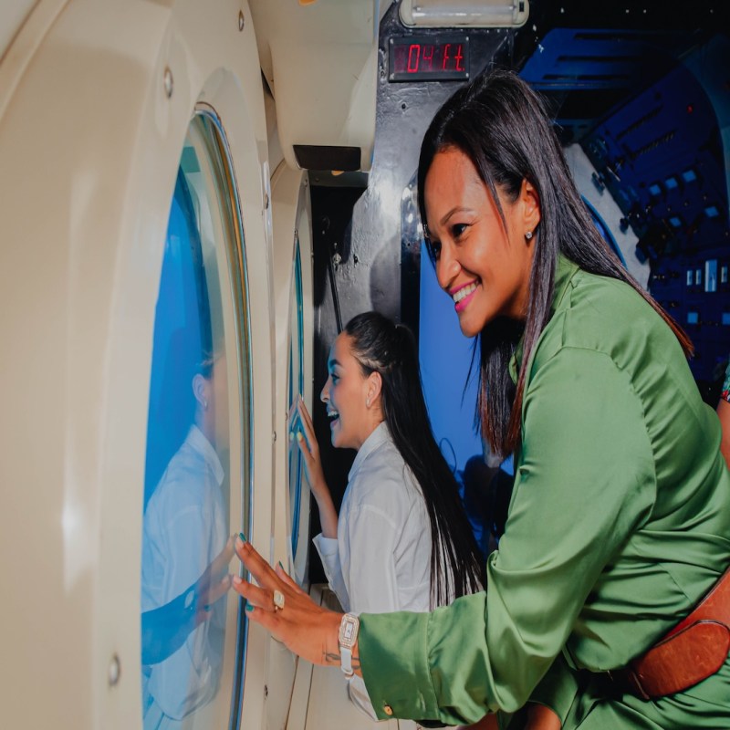 Two women smiling and looking out windows inside a submarine-like interior.