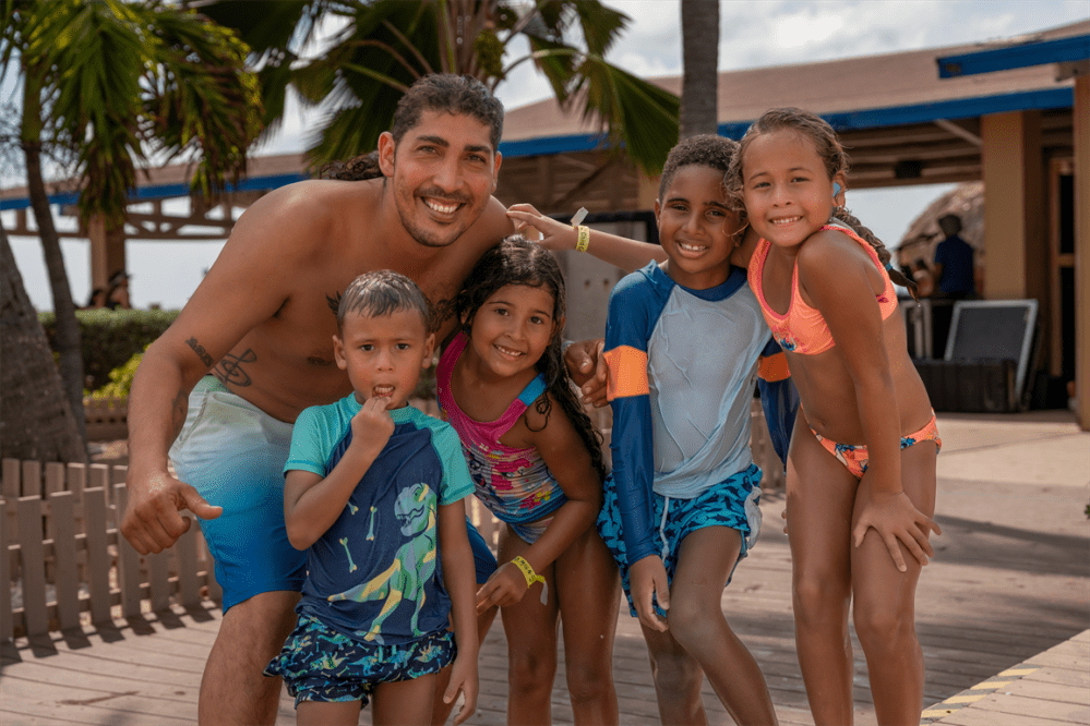 Smiling man with four children in swimwear posing outdoors by palm trees.