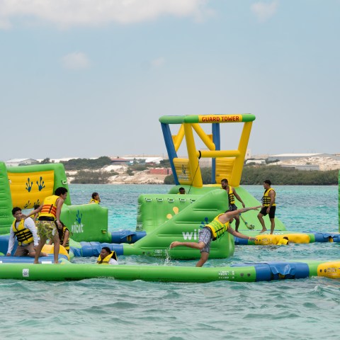 People in life jackets playing on an inflatable water park obstacle course in the sea.