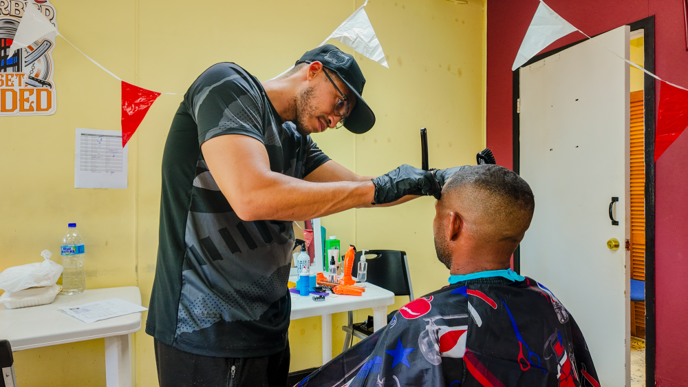 Barber in black cap giving man a haircut inside a decorated room.