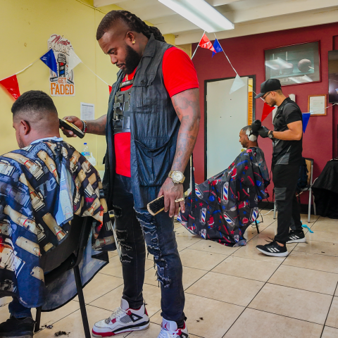 Barbershop interior with barbers cutting hair and a customer waiting.