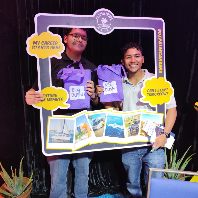 Two people holding a 'De Palm Tours Aruba' frame with bags and winning boards.