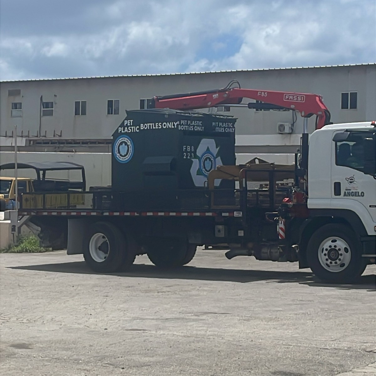 Truck with a PET plastic recycling bin and red crane parked in an industrial area.