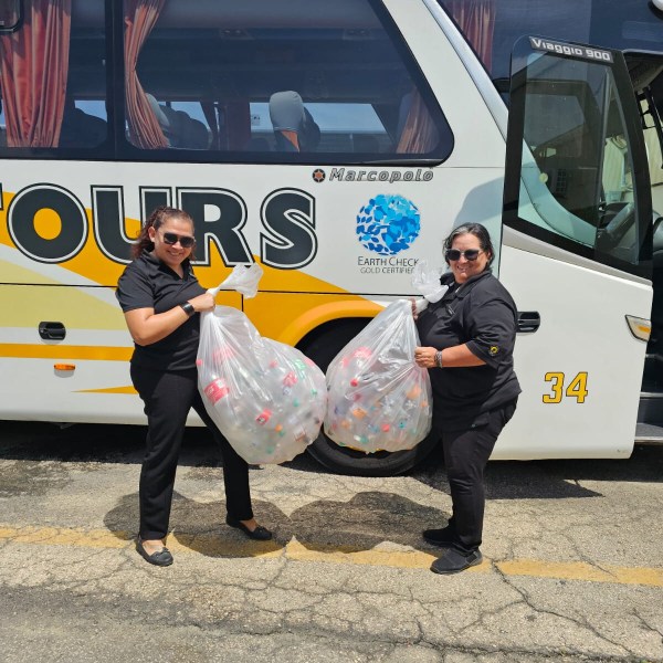 Two people holding bags of plastic bottles in front of a tour bus.