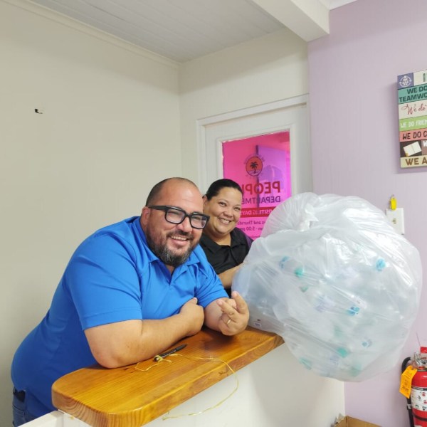 Two smiling people at a counter with a large bag of recyclables.