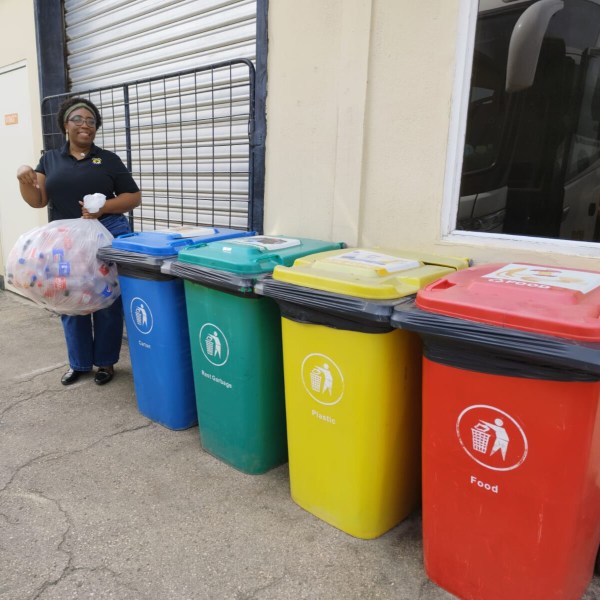 Smiling person with recyclables near color-coded waste bins for glass, plastic, and food.