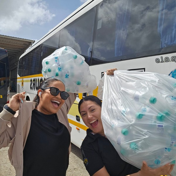 Two smiling people holding large bags of plastic bottles near a bus.