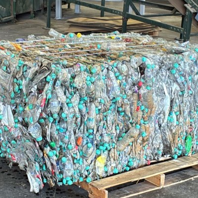 Compressed bale of plastic bottles with green caps on a wooden pallet.