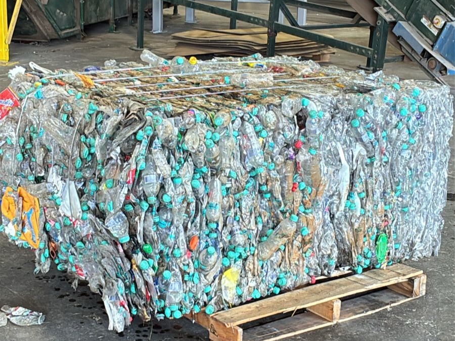 Compressed bale of plastic bottles with green caps on a wooden pallet.