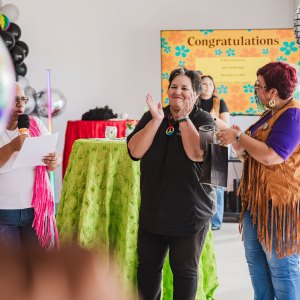 Three people during a celebration with balloons and a 'Congratulations' sign in the background.