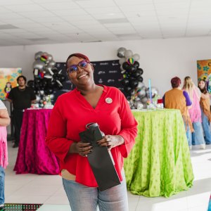 Smiling person in red shirt holds object at a colorful indoor event with balloons and decor.