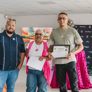 Three people posing with a certificate at a recognition event indoors, with colorful decor in the background.