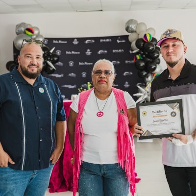 Three people pose at an event; one holds a framed certificate.