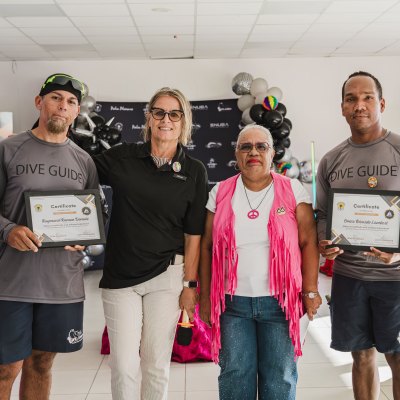 Four people pose with dive guide certificates at a recognition event indoors.