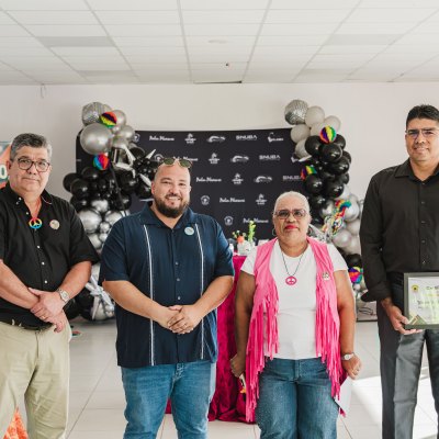 Four people standing together at an event with a recognition banner and balloons in the background.