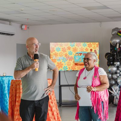 Two people speaking at an indoor event with colorful decor and a thank you slide on screen.