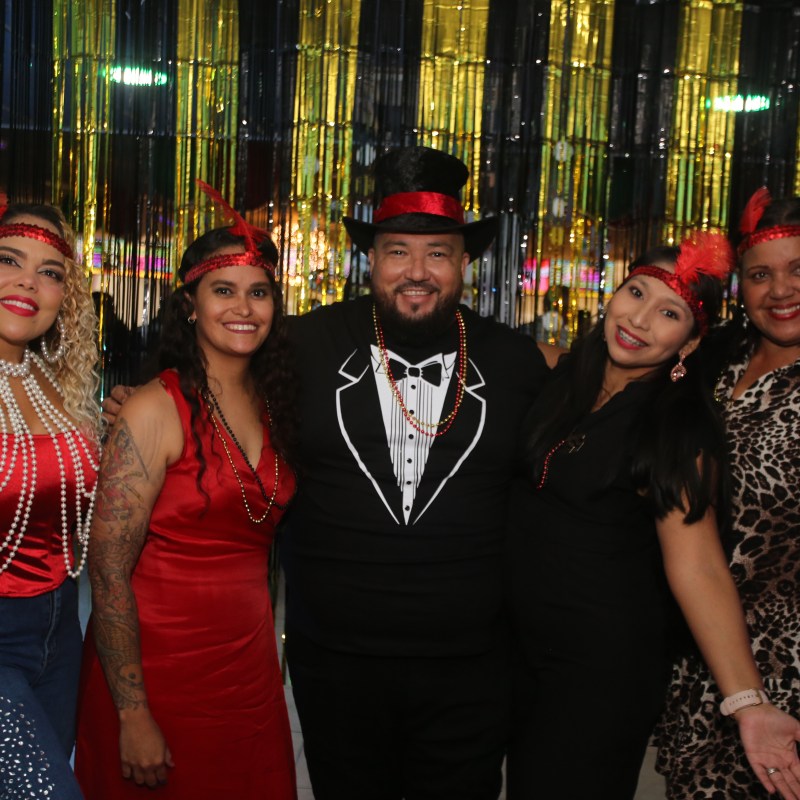 Five people in festive attire pose in front of a gold and black curtain.