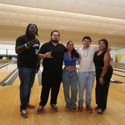 Five people posing in a bowling alley with lanes in the background.