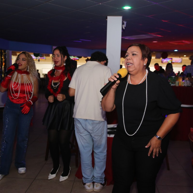 Three women in colorful outfits singing into microphones at a lively event.