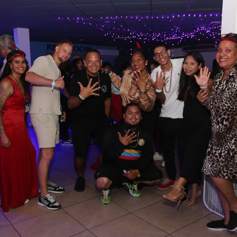 Group of people at a party, some crouching, under purple lights.