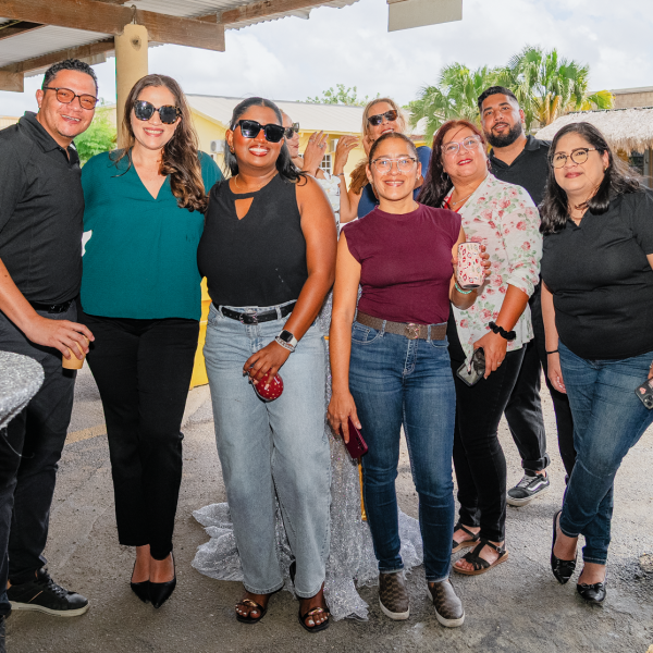 Group of eight people posing together outdoors, smiling in casual attire.