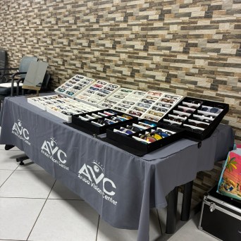Display table with various eyeglasses on trays and Aruba Vision Center branding.
