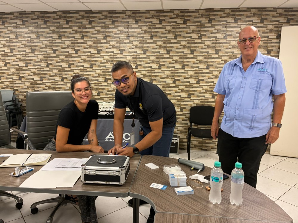 Three people smiling at a table with papers and water bottles in a conference room.