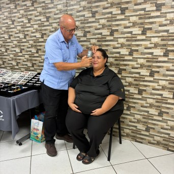 Man in blue shirt taking a photo of a seated woman against a tiled wall.