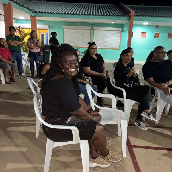Group of people seated outdoors, smiling, near a building at night.