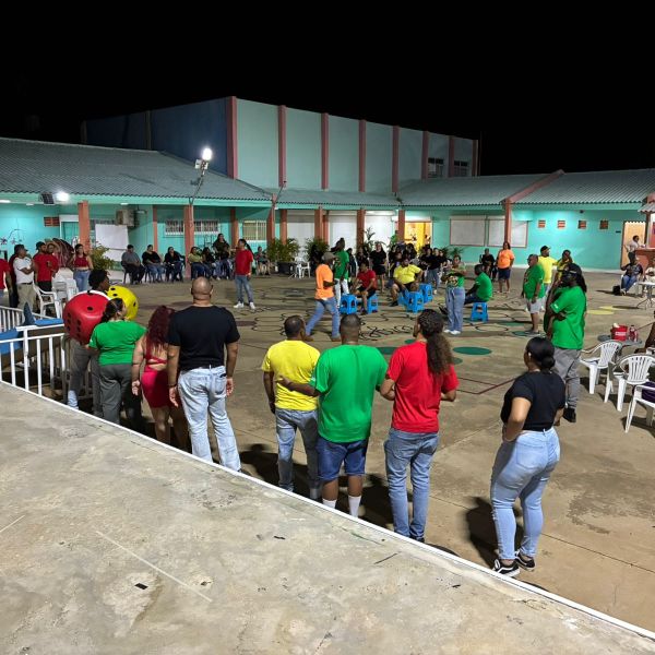 Group of people in colorful shirts gathered outside at night, playing games and sitting on plastic chairs.