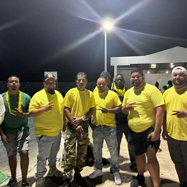 Group of nine men wearing yellow shirts and casual attire, smiling at night outdoors.